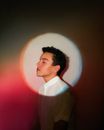 Side view of young pensive guy with closed eyes in white shirt standing near wall with neon lights