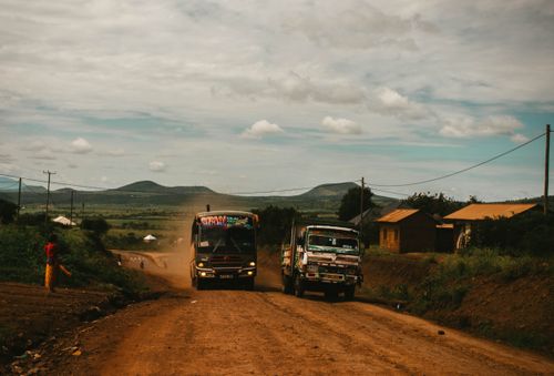 Free Vibrant trucks driving along a dirt road in rural Tanzania, with scenic hills in the background. Stock Photo