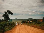 A scenic dirt road in rural Tanzania with vehicles and pedestrians under a cloudy sky.