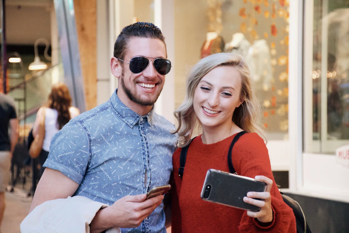 Cheerful young couple using smartphone in modern mall
