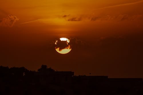 Free Silhouettes of buildings and trees under orange sky with shining sun in clouds Stock Photo