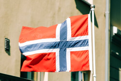 Flag of Norway with white blue and red stripes waving on flagstaff against building