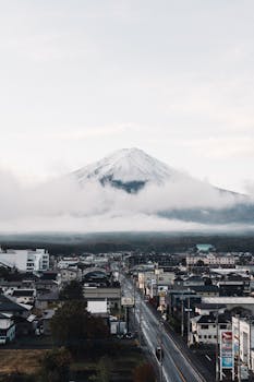 A captivating view of Mount Fuji surrounded by clouds, towering over a Japanese town with clear skies.