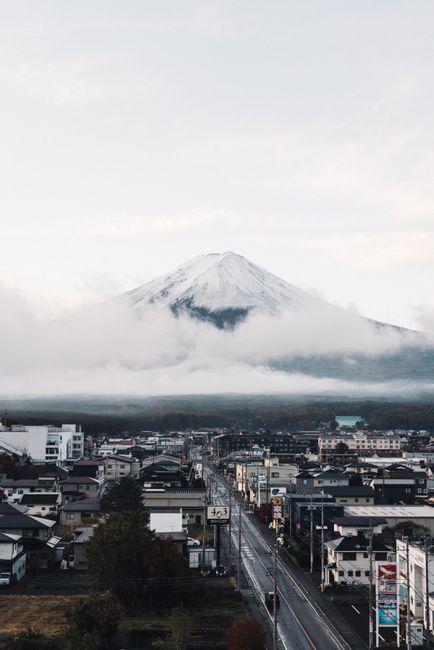A captivating view of Mount Fuji surrounded by clouds, towering over a Japanese town with clear skies.
