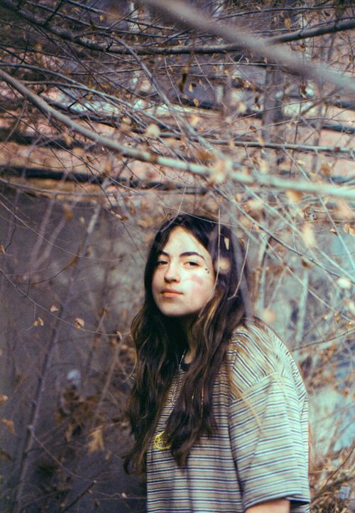 Free A young woman in a striped shirt stands in an autumnal outdoor setting surrounded by bare branches. Stock Photo