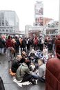 Group of people sitting in circle concrete floor on blankets in crowded street during mass event in city square during daytime