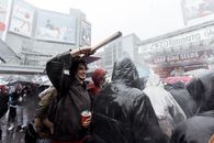 Satisfied male covering head with wooden placard while standing under rain with plastic cup amidst people during protest in city