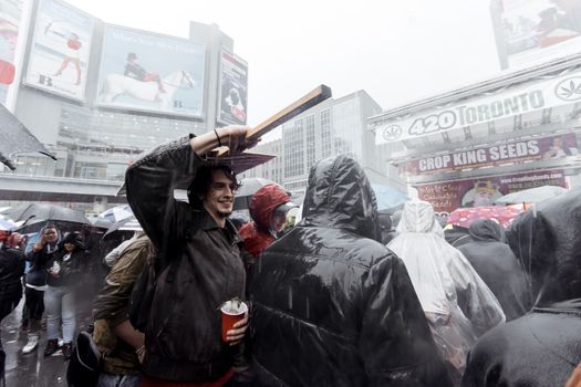 Satisfied male covering head with wooden placard while standing under rain with plastic cup amidst people during protest in city