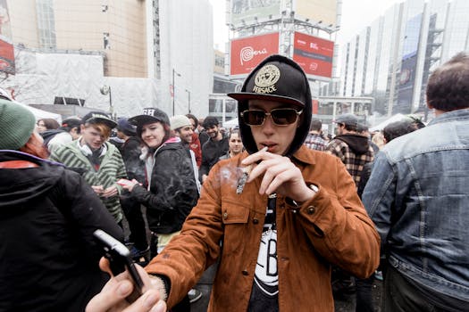 一个戴着帽子和兜帽的年轻人，站在市中心的拥挤街道上，手里拿着智能手机，正在抽大麻
