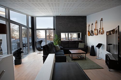 Free Contemporary living room with comfortable sofa and armchair near table located next to big windows against guitars on wall inside Stock Photo