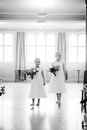 Black and white of girls in elegant dresses with bridal bouquets in registry office during wedding ceremony in light room