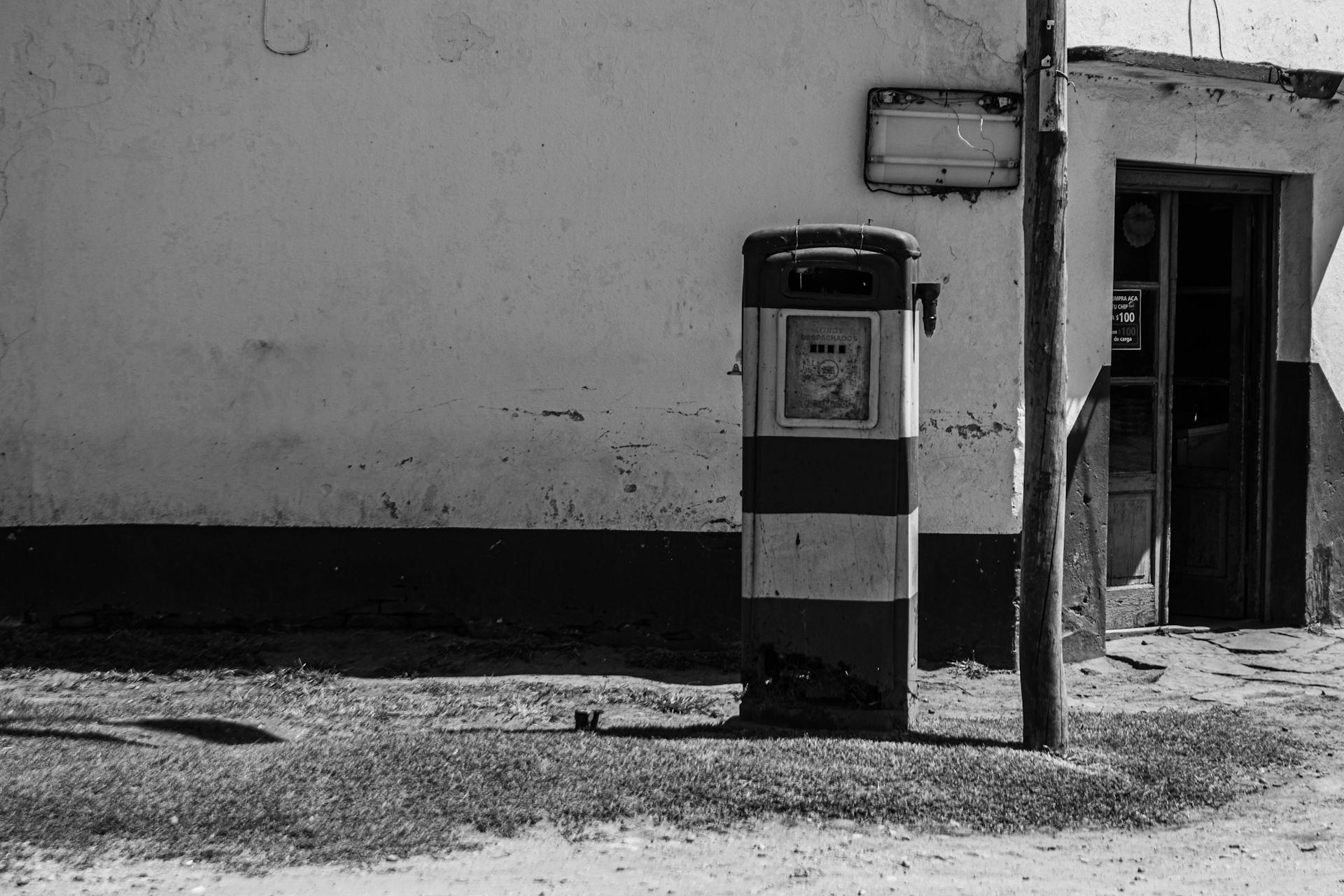 Weathered vintage gas station exterior with old pump and wall in black and white.