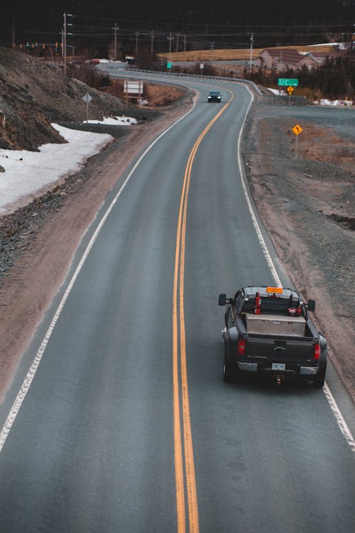 From above of black automobile driving on highway with marking lines near snowy roadside in city during daytime in countryside