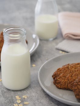 A comforting breakfast setup with oatmeal cookies and bottles of milk on a neutral background.