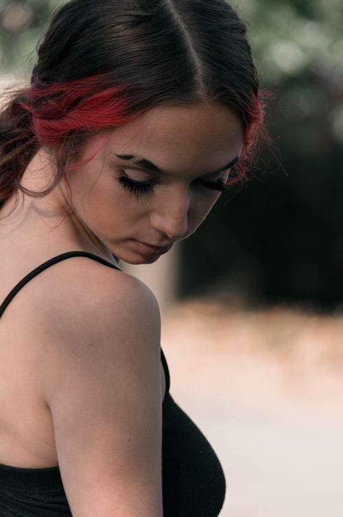 Free Serious young female in black top and bunch looking down in daylight on blurred background Stock Photo