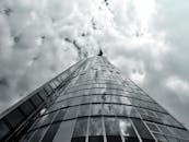 在阴沉的天空下，以低角度拍摄一座高耸的现代玻璃摩天大楼，展现出建筑的未来主义风格