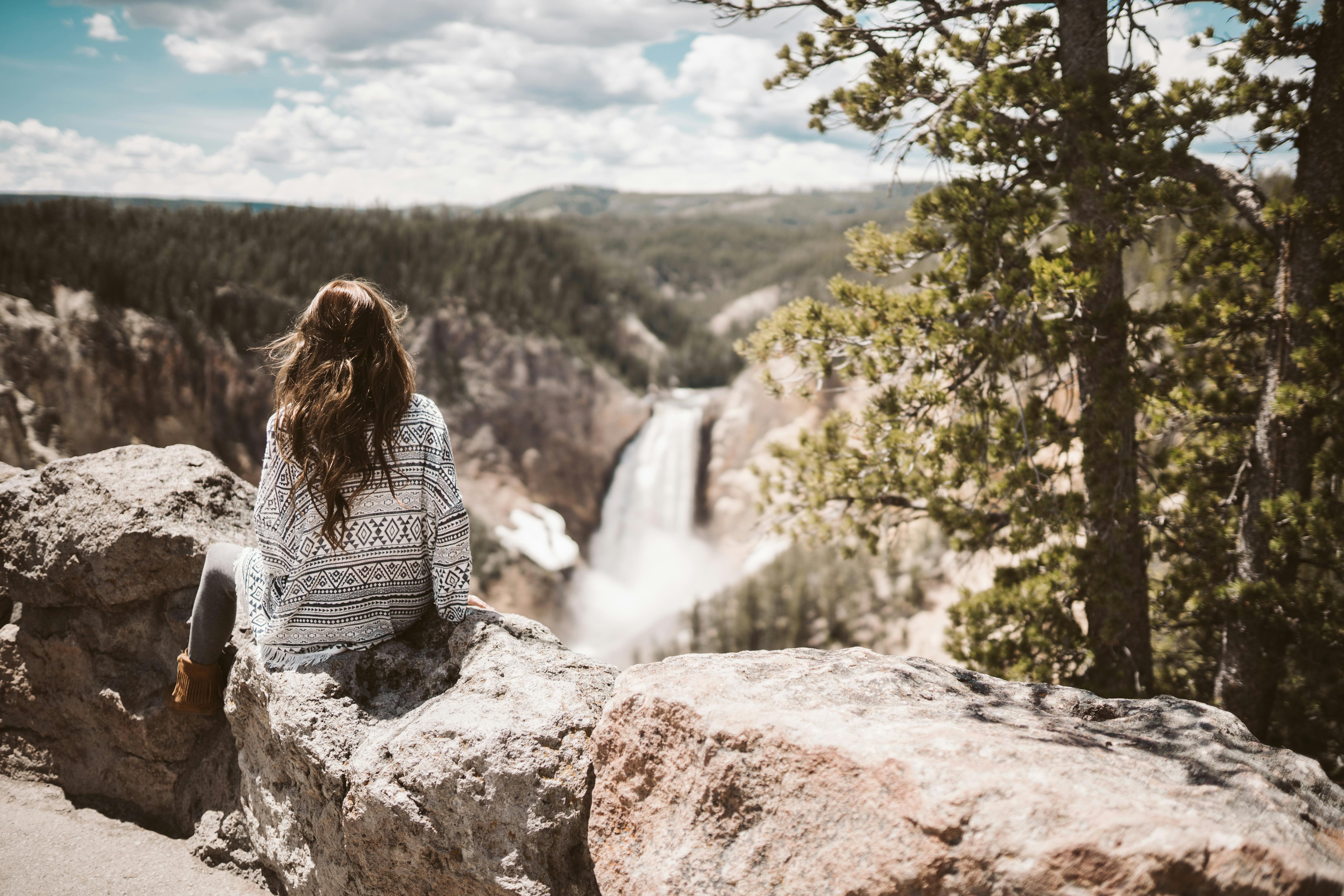 A woman sitting on rocks enjoying the scenic view of a waterfall in the Grand Canyon, under a bright summer sky.