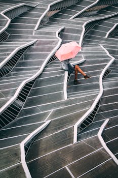 Woman holding a pink umbrella sitting on a geometric metal staircase