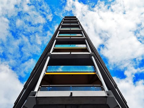 从低角度俯瞰现代玻璃建筑，蓝天之上云层散落