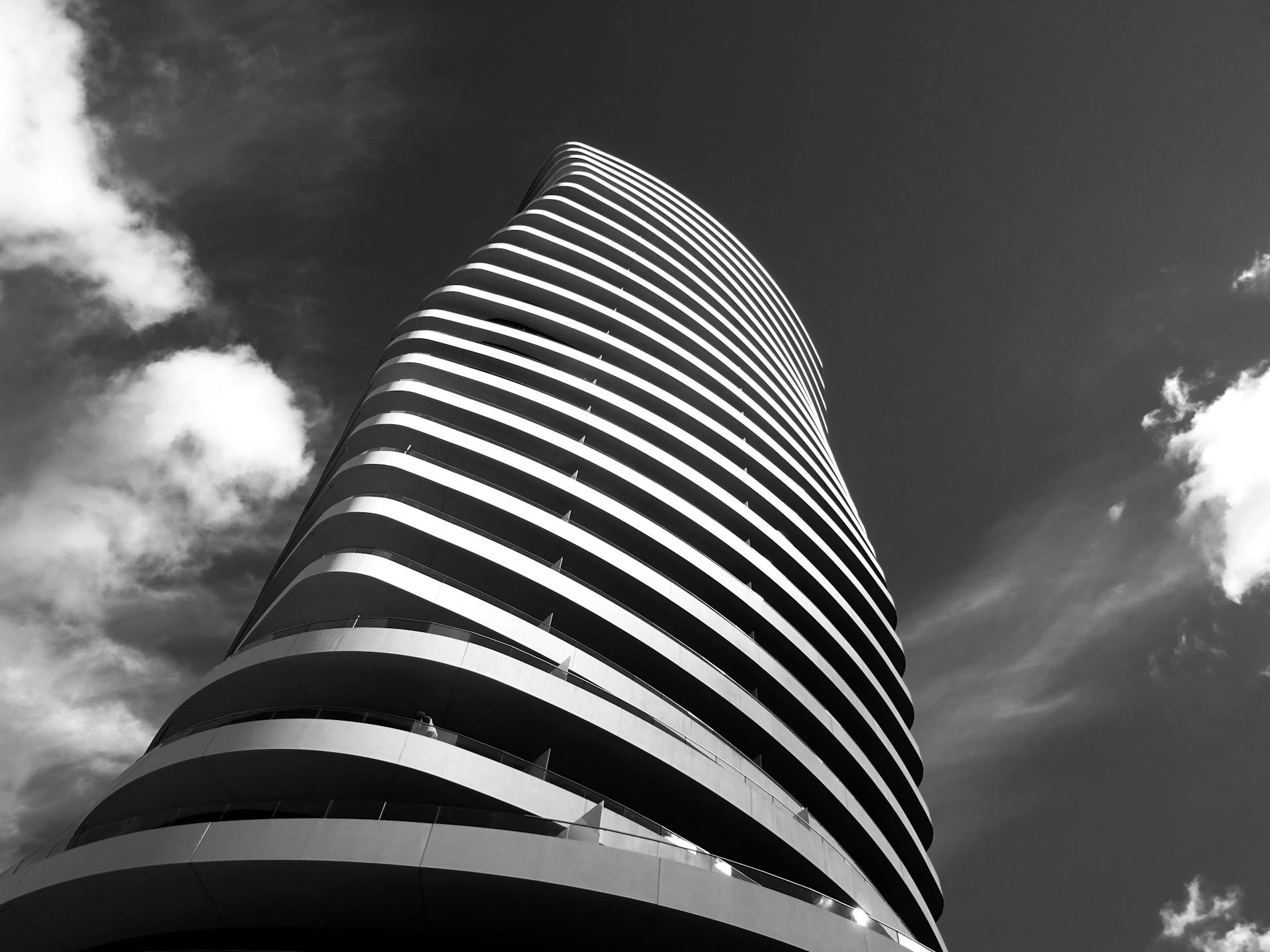 Modern skyscraper with curved design and glass elements against a cloudy sky.