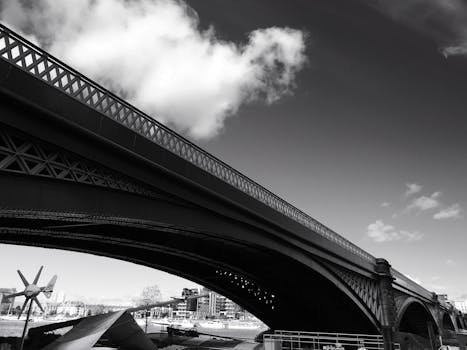 这张黑白照片从低角度拍摄，捕捉了一座大型城市桥梁的引人注目建筑细节