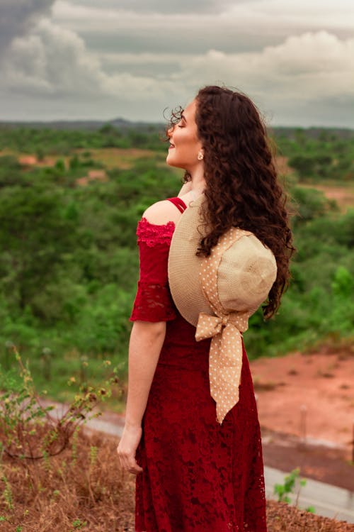Back view of anonymous young dreamy female with closed eyes and wavy hair under cloudy sky