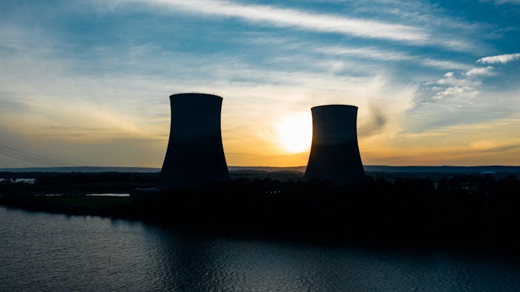 Similar Cooling Towers Near Lake Under Bright Sky At Sunset