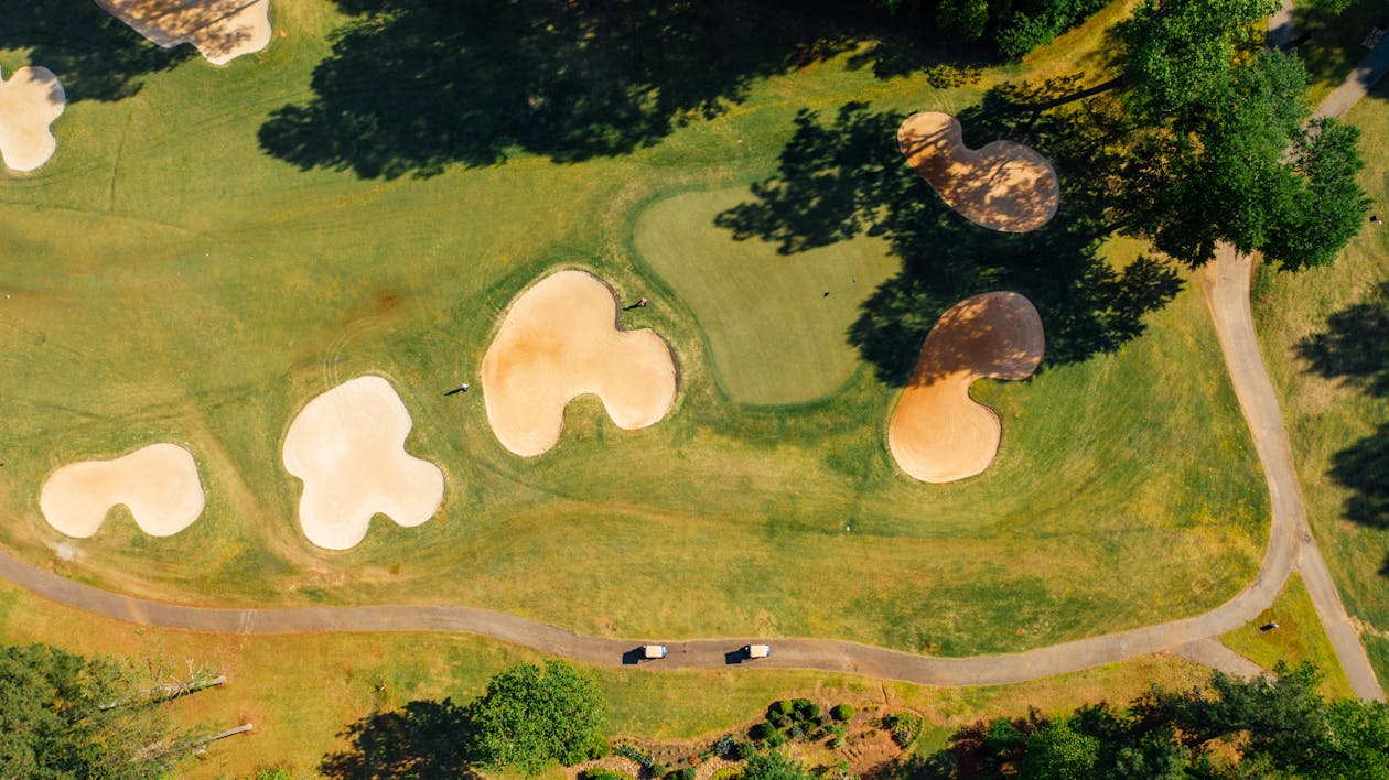 Free Aerial view of grass golf course with sandy bunkers near trees and narrow roadway in countryside Stock Photo