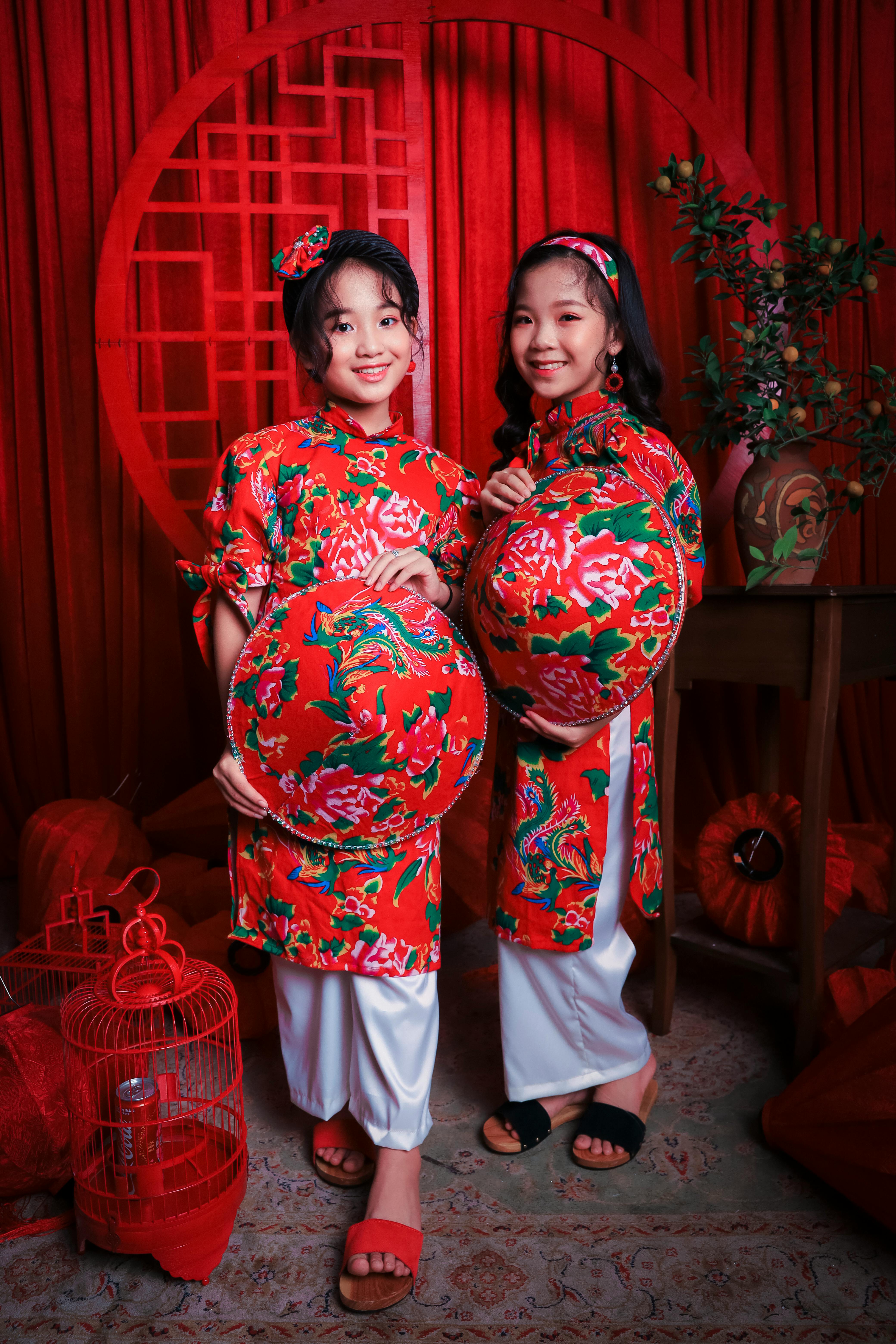 Content ethnic kids in traditional wear and sandals standing with bright hats on rug while looking at camera