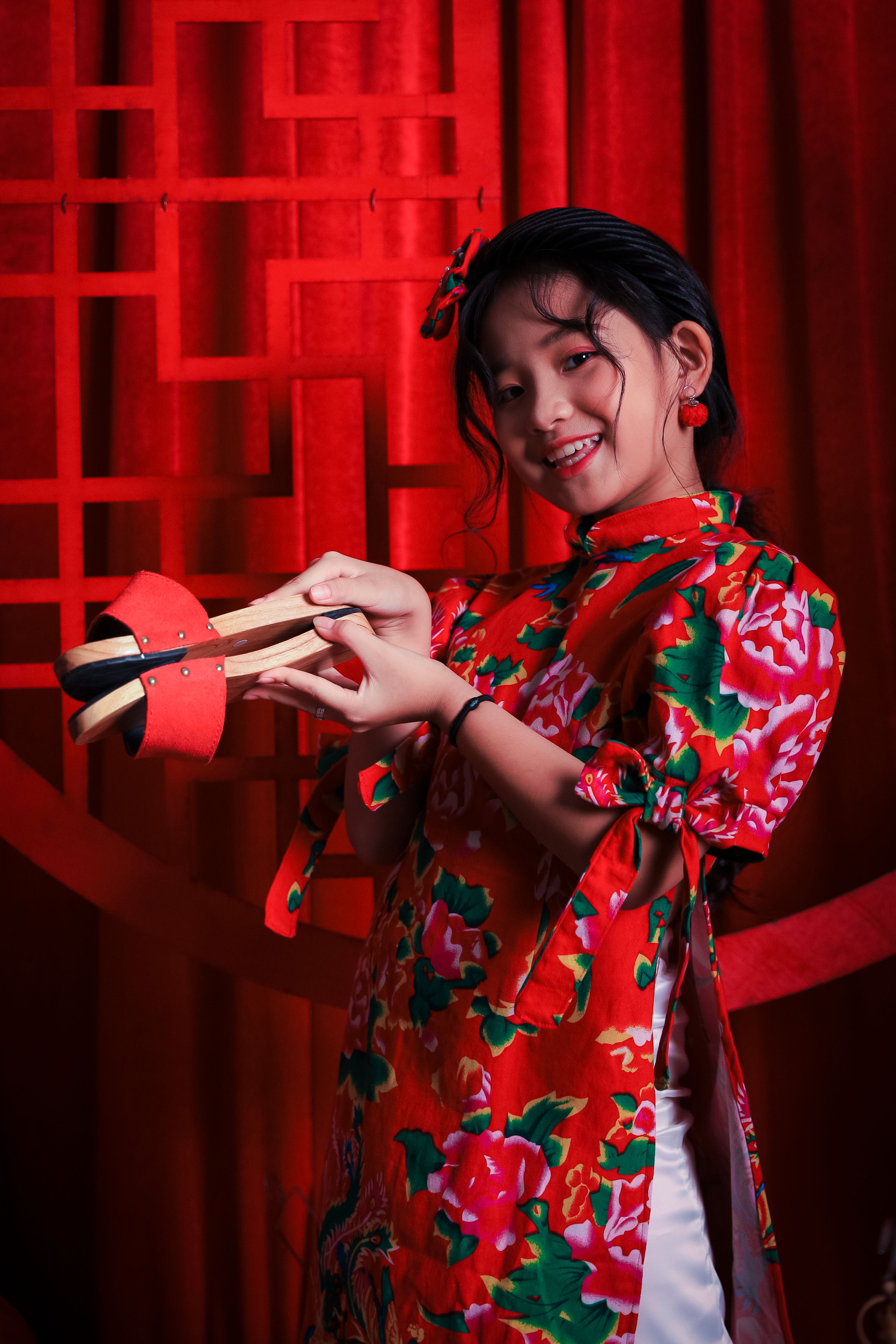 一位穿着红色花卉连衣裙的亚洲女孩，在节日背景下微笑着手持传统鼓