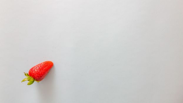 A single fresh strawberry on a white background, ideal for food and health themes.
