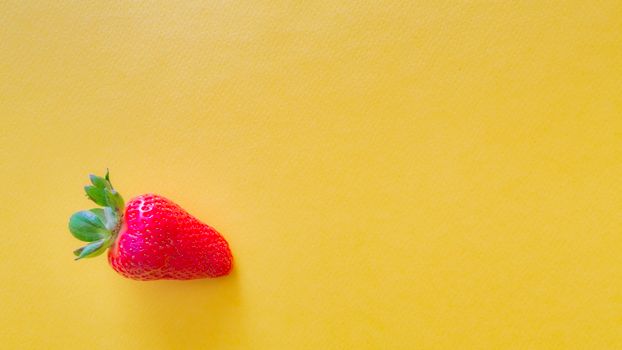 A vivid close-up of a fresh strawberry on a bright yellow background.