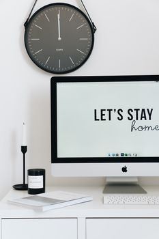 Clean and minimalist home office desk featuring a clock, monitor with 'Let's Stay Home' text, and decor.