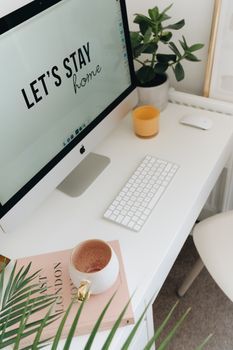 Modern home office desk with computer, keyboard, plants, and a cup of coffee for a cozy work environment.