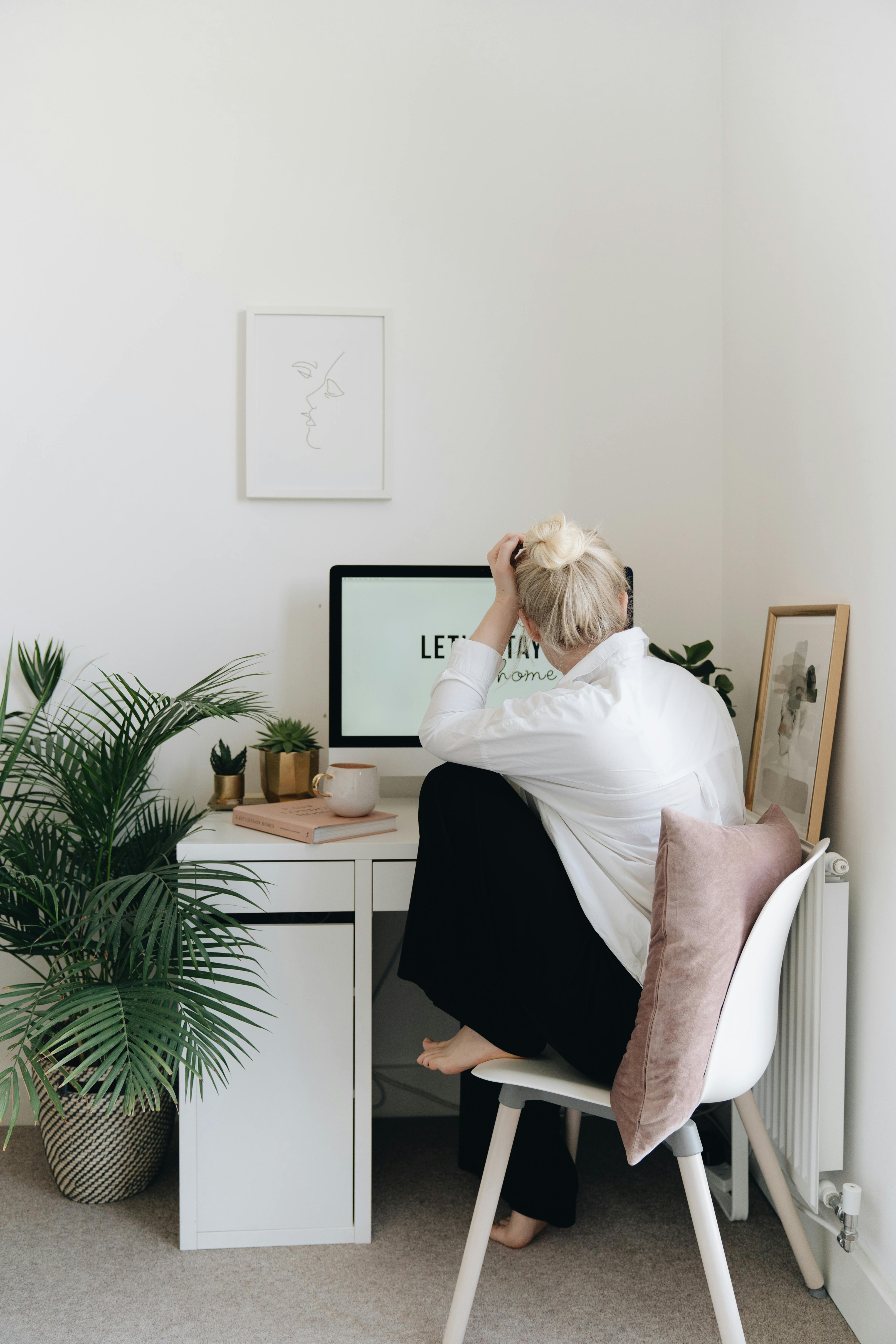 Free Minimalist home office with person sitting by desk, plants, and neutral decor. Stock Photo