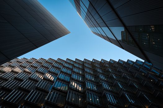 Low angle view of modern skyscrapers with glass panels reflecting under a blue sky.