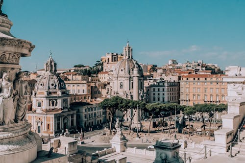 From above of aged masonry churches near houses and statues under blue cloudy sky in Italy