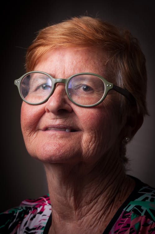 Free Smiling senior female with red head and wrinkled skin in eyeglasses looking at camera on gray background Stock Photo