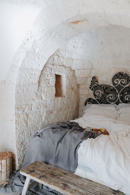 Inviting rustic bedroom featuring stone walls, a wrought iron bedframe, and cozy bedding.