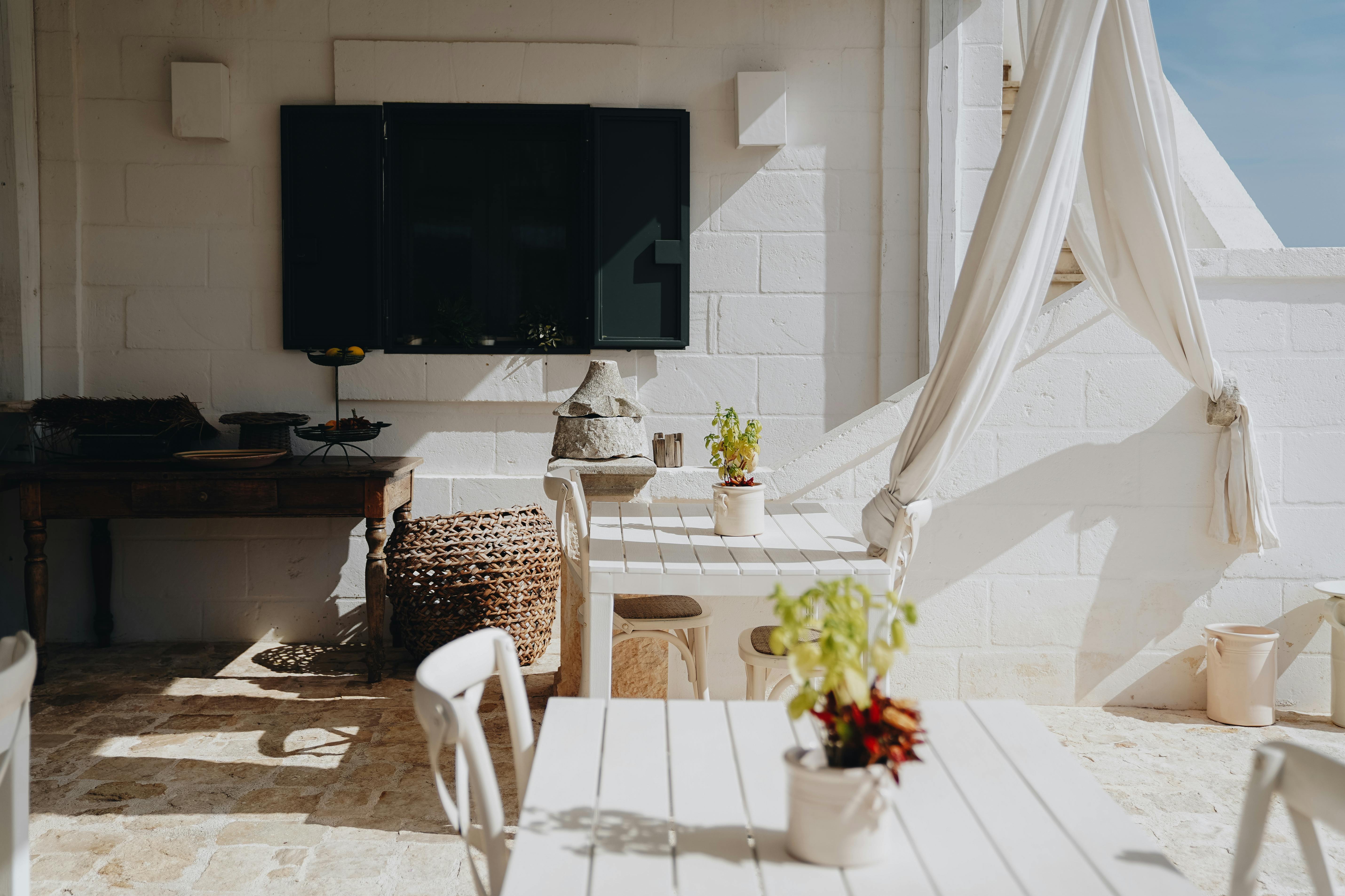 Elegant outdoor patio space featuring white furniture, plants, and soft lighting under a bright sky.