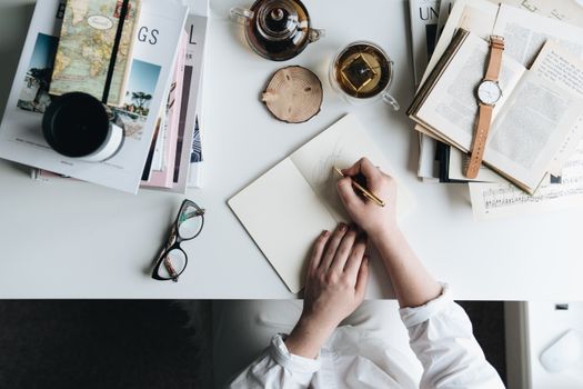 A cozy flatlay of a workspace with a notebook, cup of tea, and open books for creative writing.
