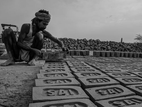 Free Black and white ground level of poor barefoot ethnic male in head wear squatting while putting bricks with carved letters on dry terrain Stock Photo