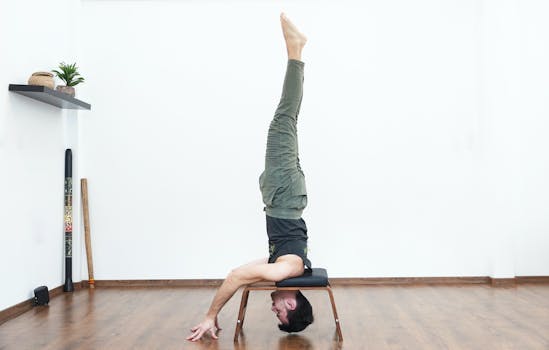 Adult man performing a headstand on a stool in a minimalist indoor setting, showcasing fitness and balance.