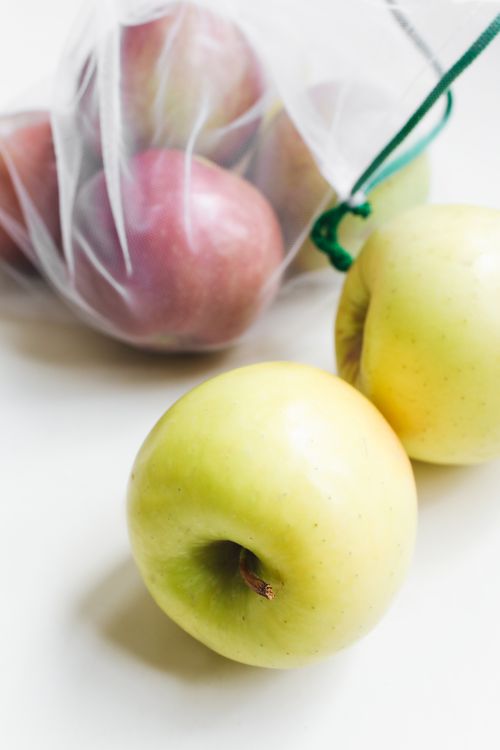Free Close-up of fresh green apples with red apples in a reusable mesh bag on a plain background. Stock Photo