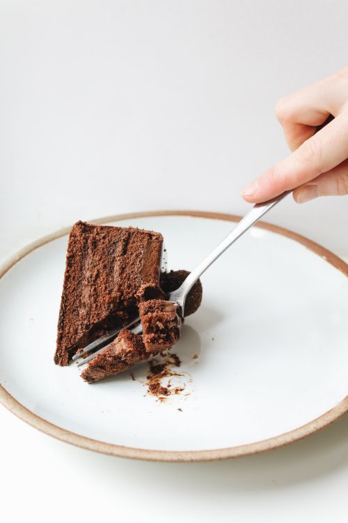 Free Close-up of a hand using a fork to slice a piece of chocolate cake on a plate. Stock Photo