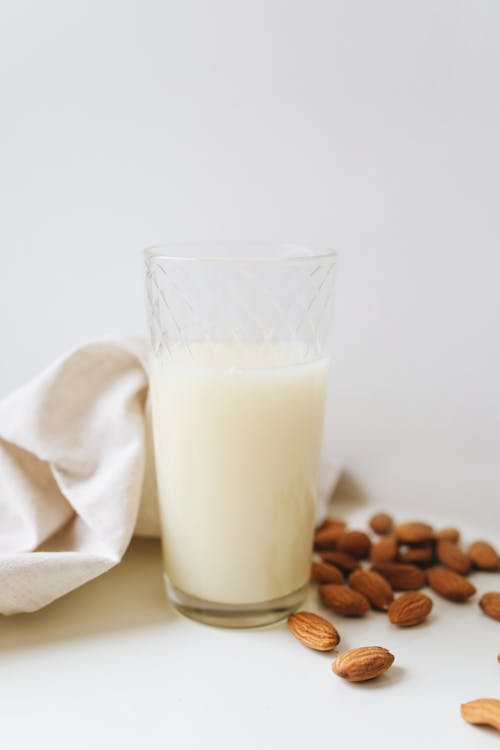 Milk in Clear Drinking Glass Beside Brown Coffee Beans