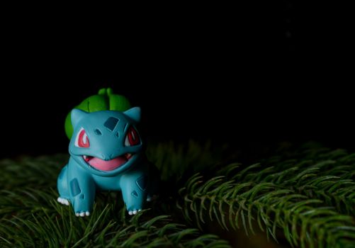 Vibrant Bulbasaur toy placed on pine needles with a dark background.