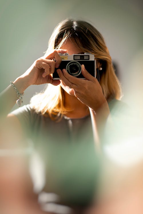Anonymous female in casual wear with wristband taking photo on modern camera in sunlight in back lit