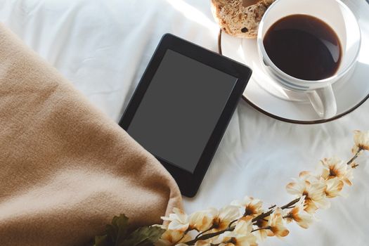 Comforting setup with coffee, tablet, and flowers on a bed, ideal for a relaxed morning.