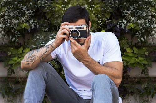 Unrecognizable hipster male photographer taking photo on camera near tree